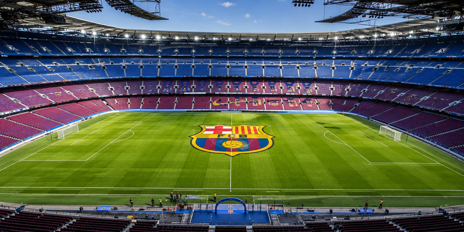 Estádio de futebol com o escudo do Barcelona no centro do campo e arquibancadas em azul e grená.